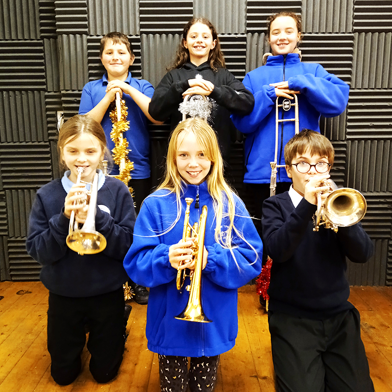 6 young, white chilren wearing uniform and holding brass instruments.