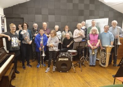 A group of adults and young people stand with their brass instruments in a band room