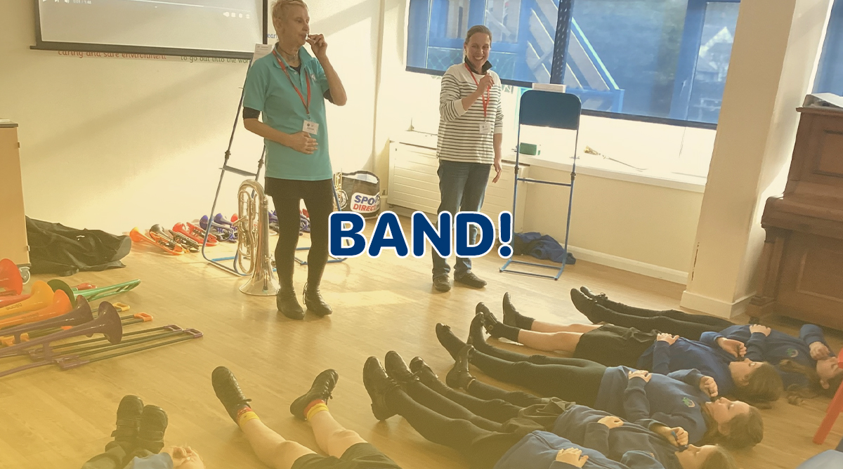 A group of adults and young people stand with their brass instruments in a band room