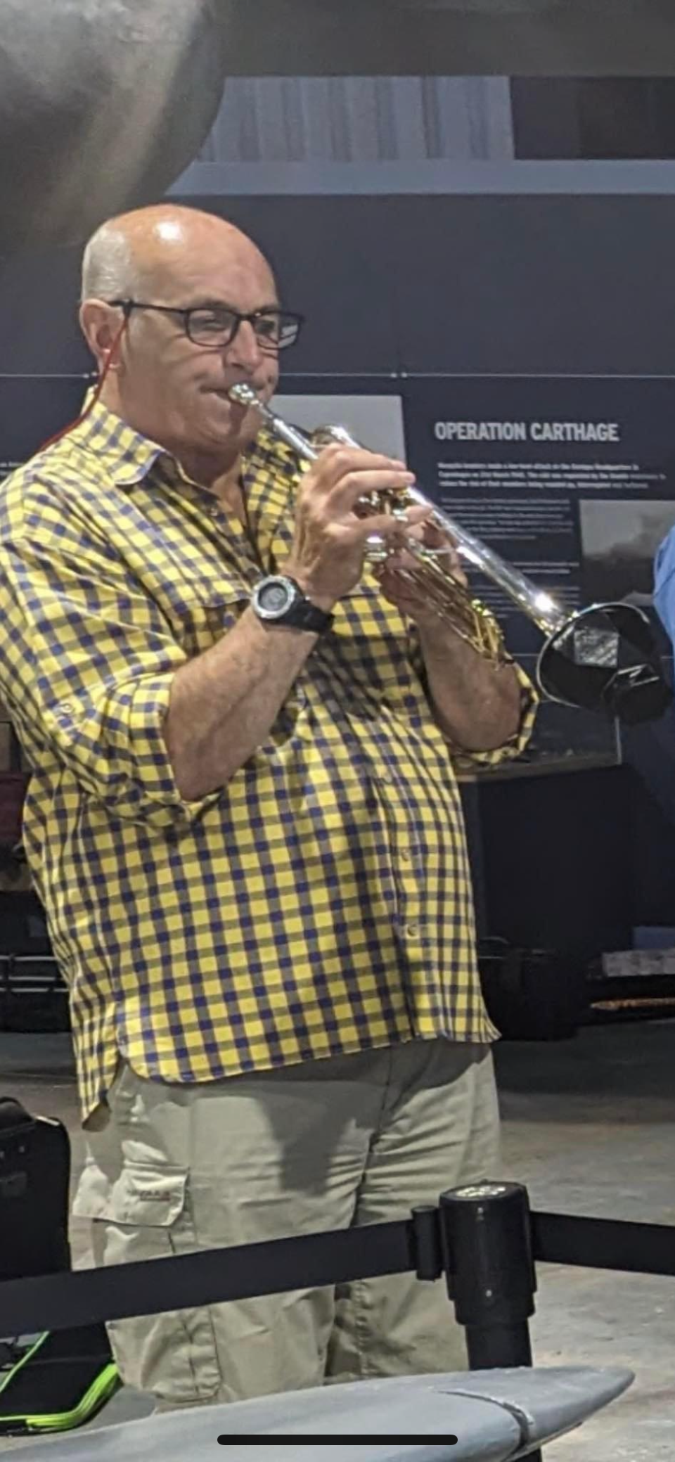 A white man, bald on top, plays a trumpet