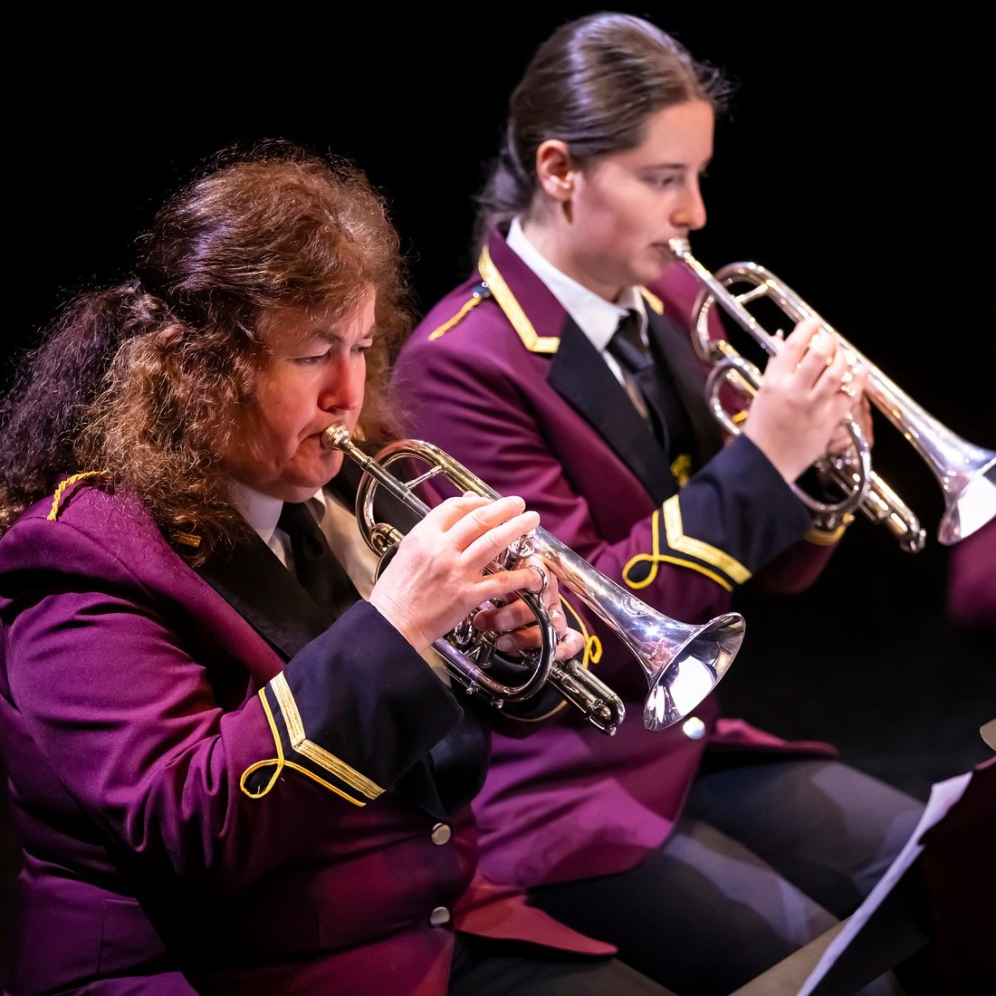 A white man, bald on top, plays a trumpet