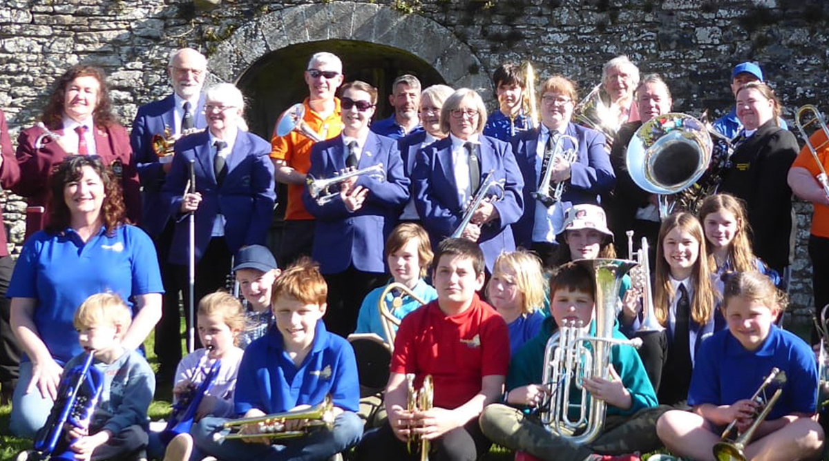A group of adults and young people stand with their brass instruments in a band room