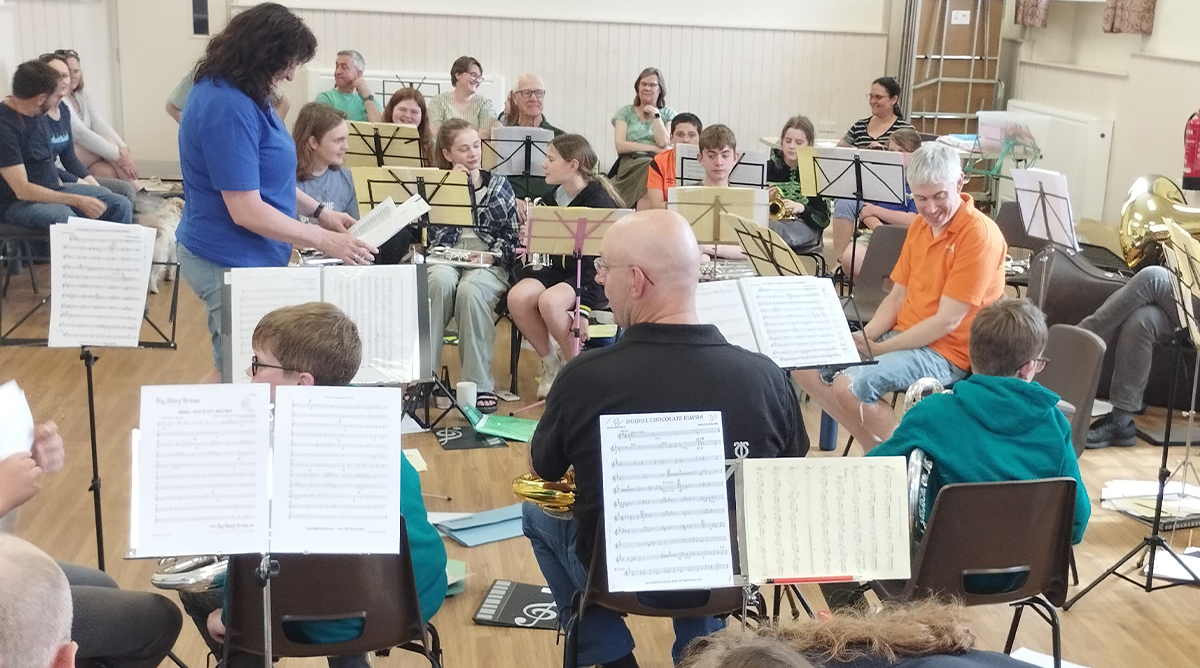 A group of adults and young people stand with their brass instruments in a band room