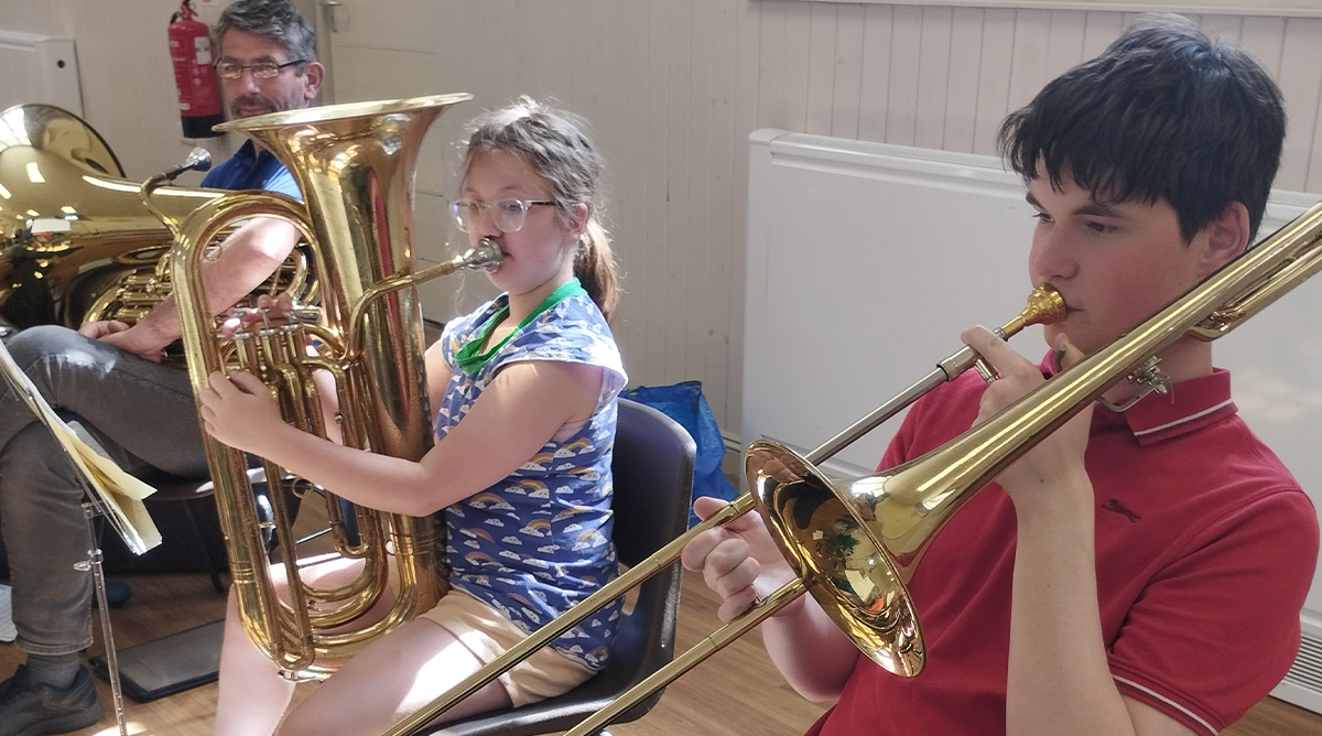 A group of adults and young people stand with their brass instruments in a band room