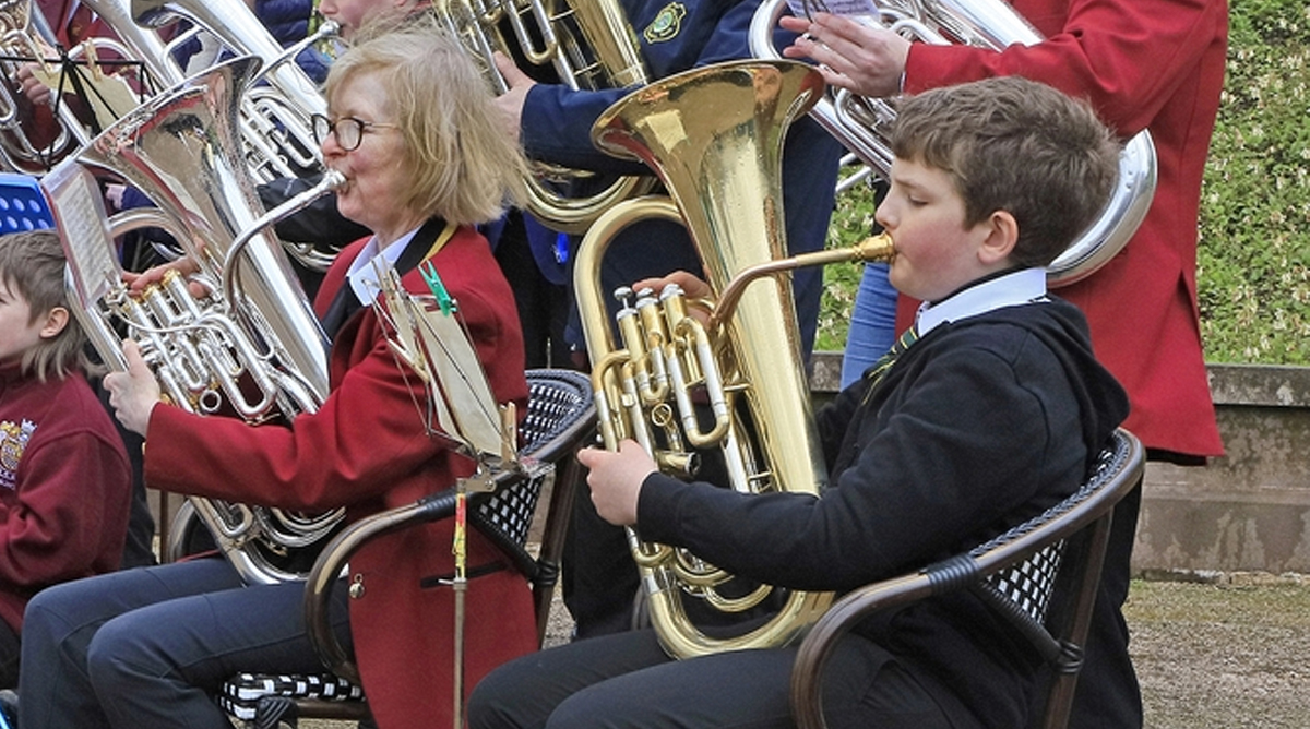 A group of adults and young people stand with their brass instruments in a band room